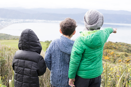 Three tamariki overlooking a bay and pointing