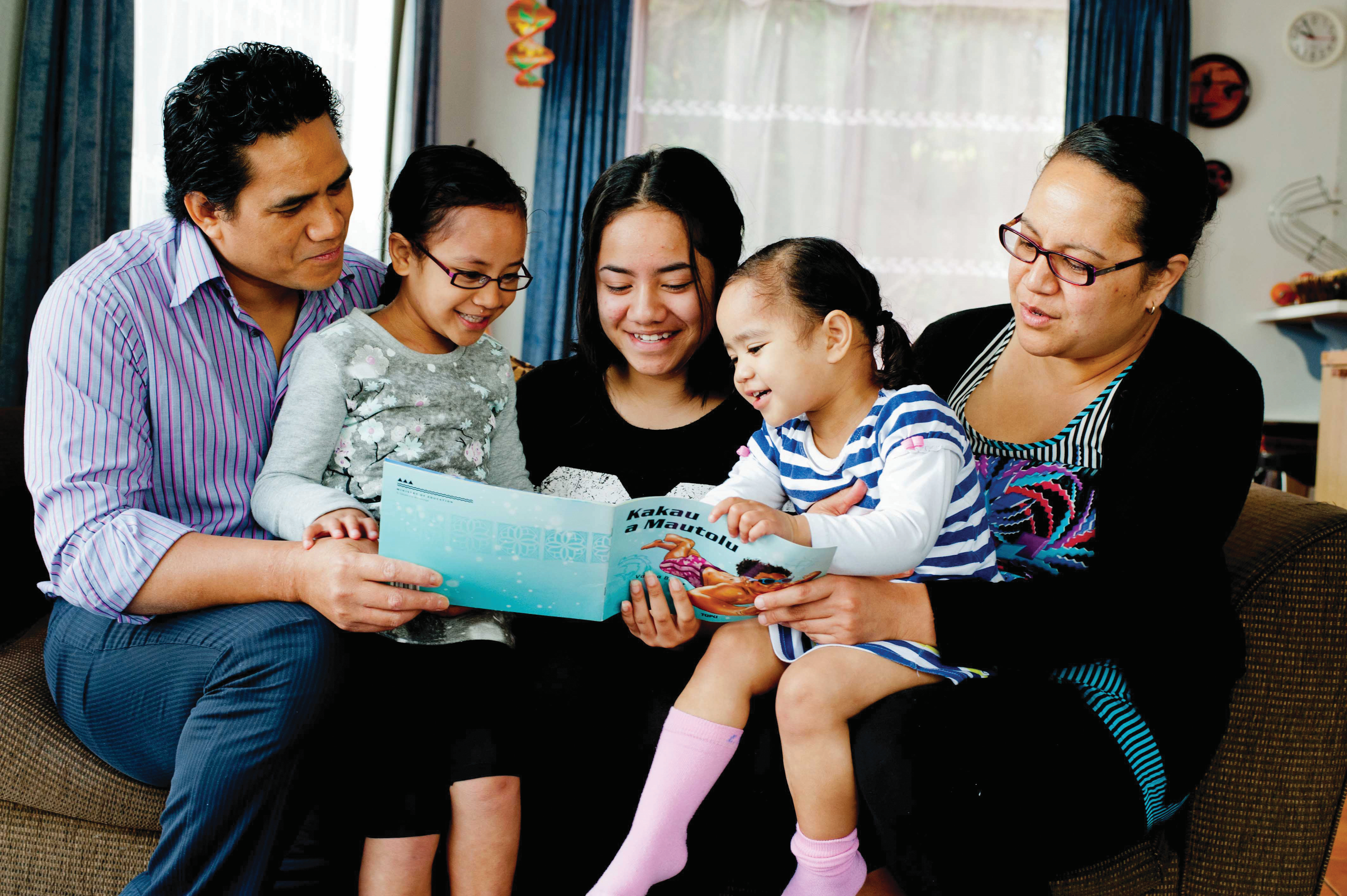 Family sat on a couch reading a book together.