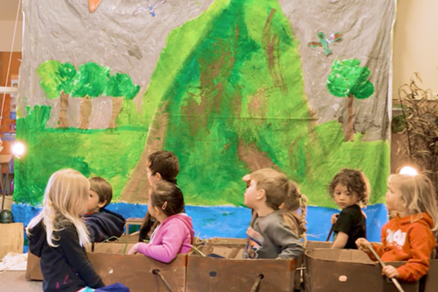 Children sitting in make-believe waka made of boxes