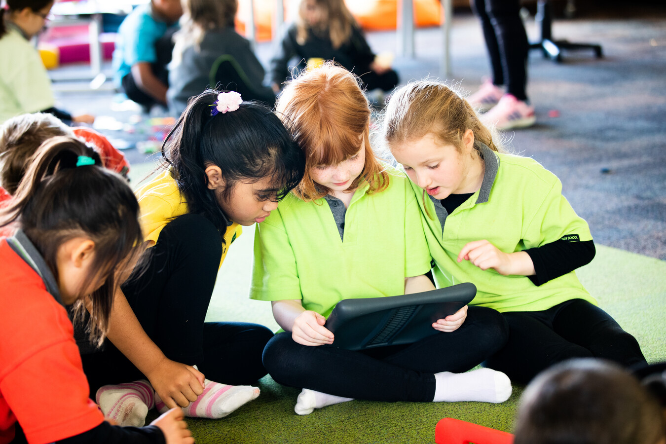 Students sitting together on a mat, working on a computer tablet.