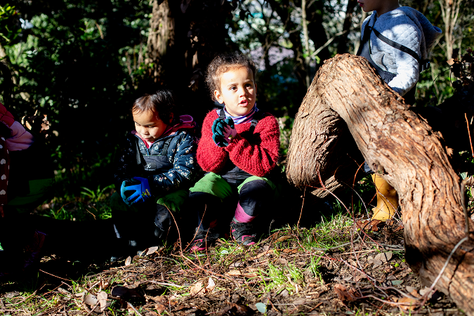 Two children sitting by a tree in the bush