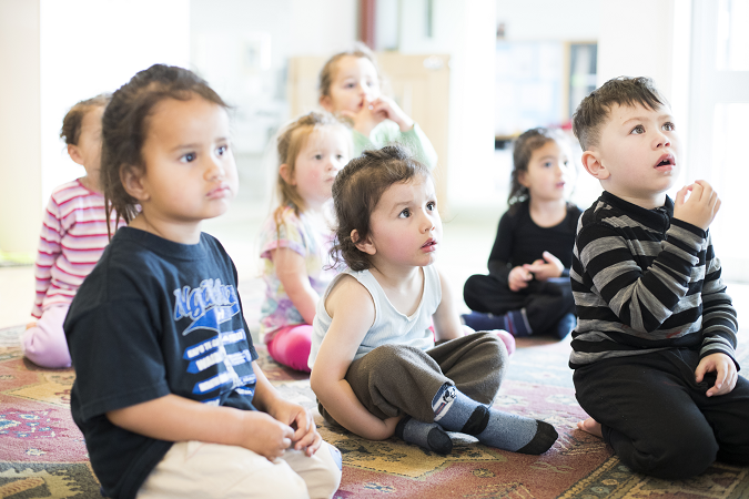 A group of tamariki sit on the floor listening to their kaiako.