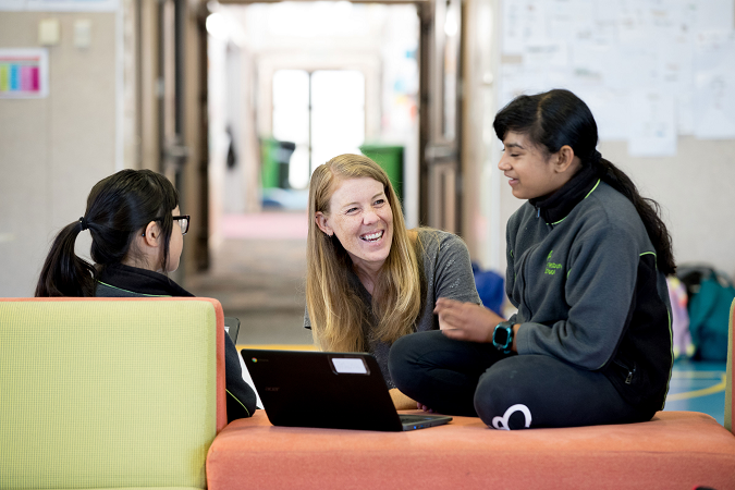 Kaiako and two students sit together smiling as they work on laptops. 