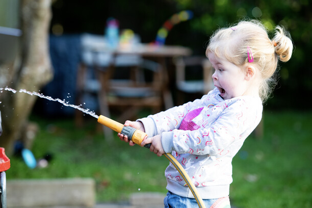 Little girl playing with garden hose.