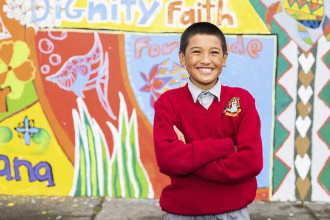 Boy in school uniform standing and smiling with arms folded.