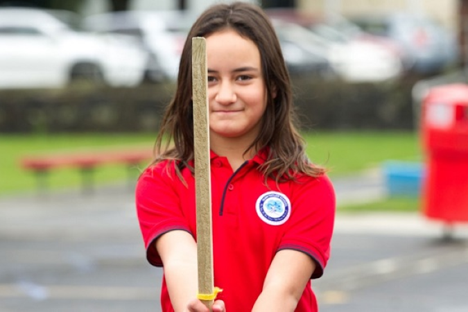 Student smiles at the camera holding up a wooden stick. 