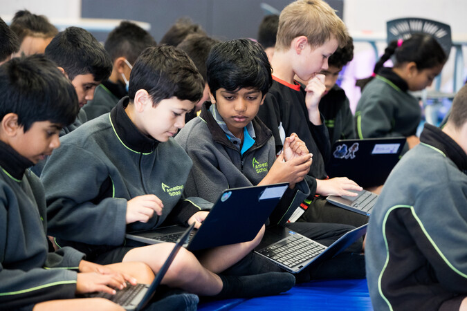 A group of students sit together working on their laptops.