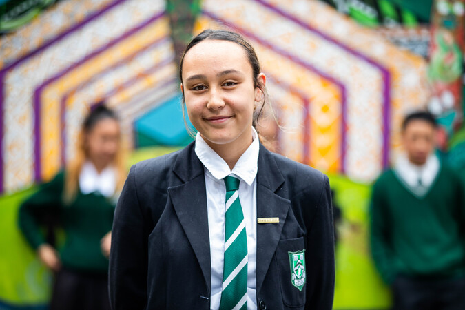 Tamariki stands in school uniform, smiling at the camera.