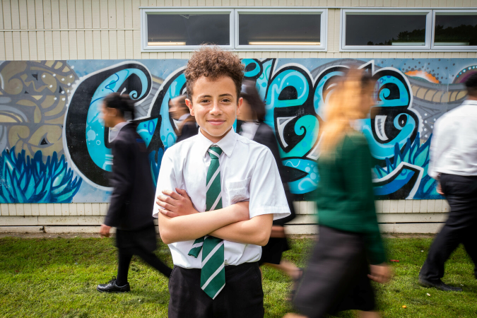 Student standing with arms folded as classmates walk pass between them and a mura