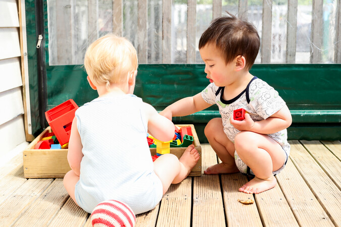 Two babies playing with toys on a deck