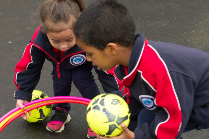 Two children playing with footballs and hula hoops together. 