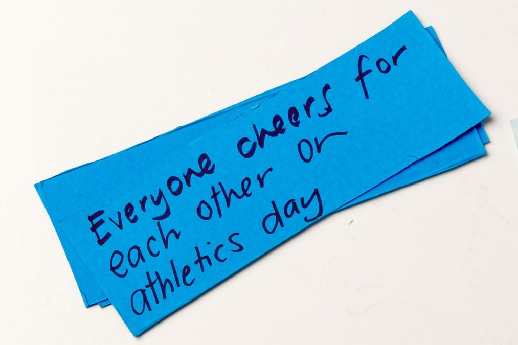  Blue card with the words "Everyone cheers for each other on athletics day". 