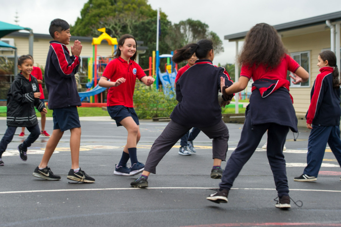 A group of tamariki are playing tag rugby on the courts.