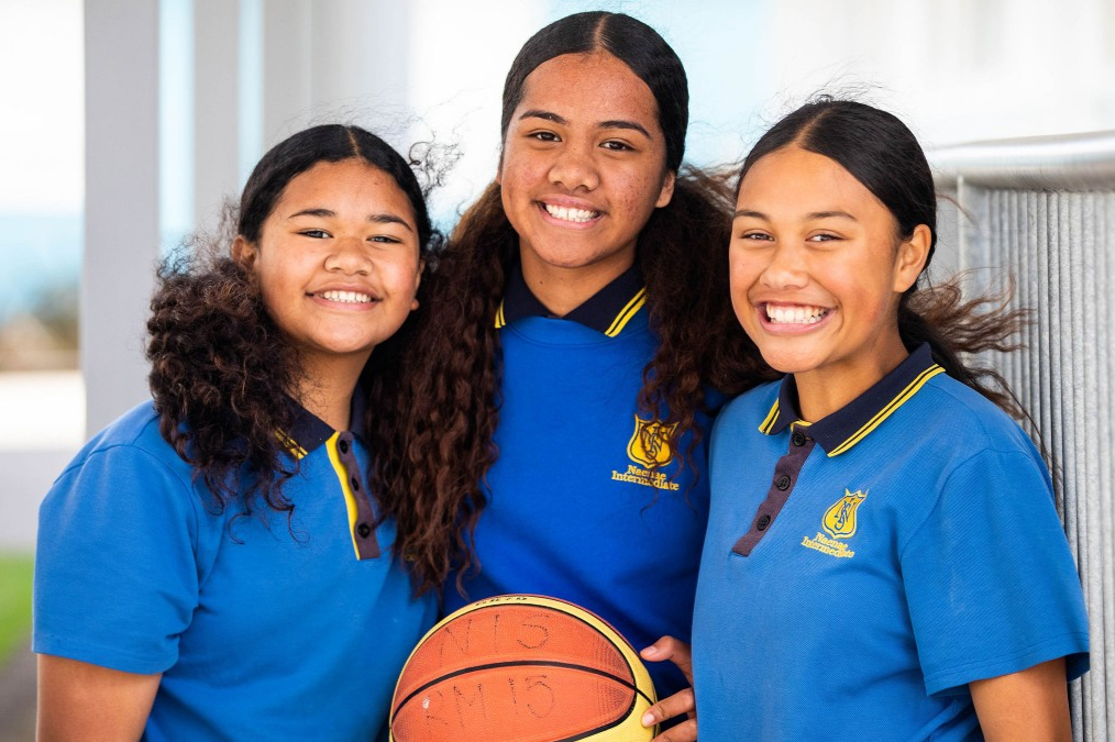 Three students stood together looking at the camera and holding a basketball.