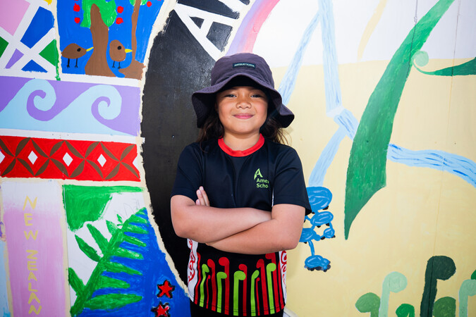 Child standing in front of a mural smiling.