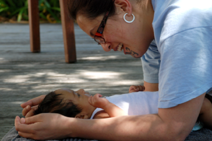 Wahine and a pēpē lying on a deck in the shade making eye contact