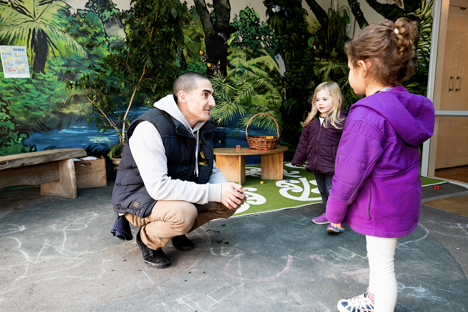 A man kneeling down and talking at two children