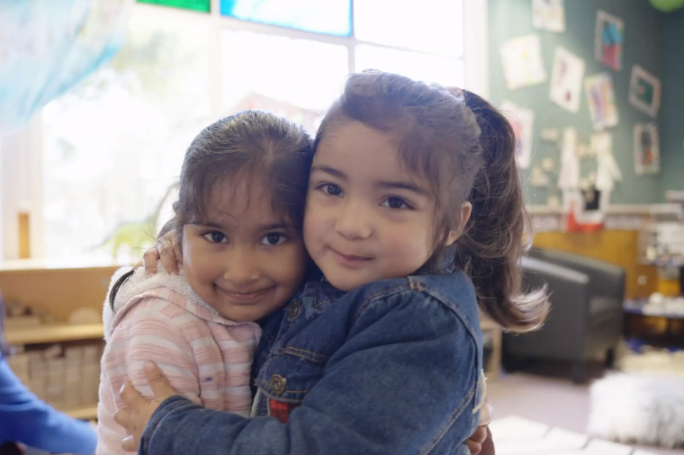 Two girls hugging each other while smiling at the camera