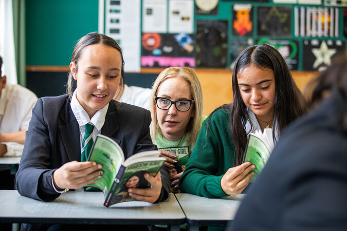 Teacher sits and reads a book with her students.