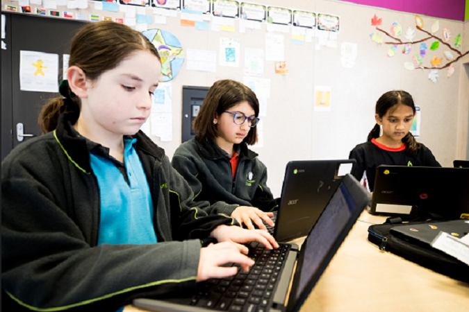 Three ākonga sit together at the table in their classroom working on laptops.