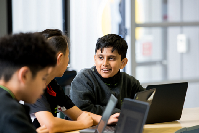 Ākonga sits at their desk working on their laptop.