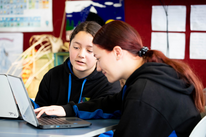 Two ākonga sit together in the classroom working on laptops.