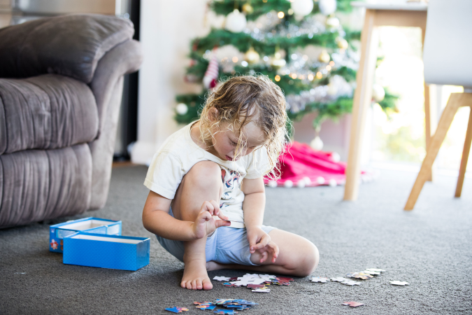 Small child sitting on grey carpet building a puzzle