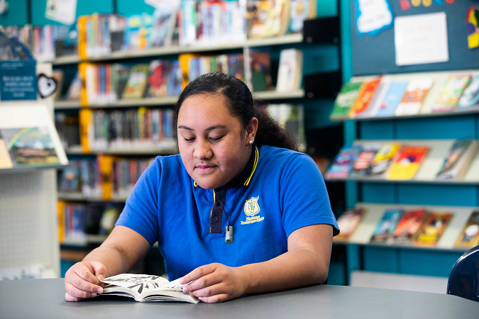 Tamariki sits in the school library reading a book. 