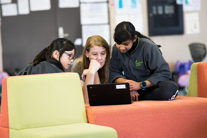 Kaiako and two students working on a laptop together.