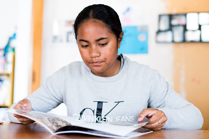 Tamariki sits at the table reading a book.