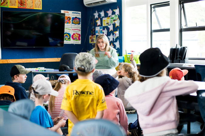 A teacher is sat ion a chair and is teaching students who are on the floor 