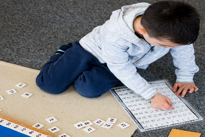 A child on the floor engrossed in a maths puzzle.