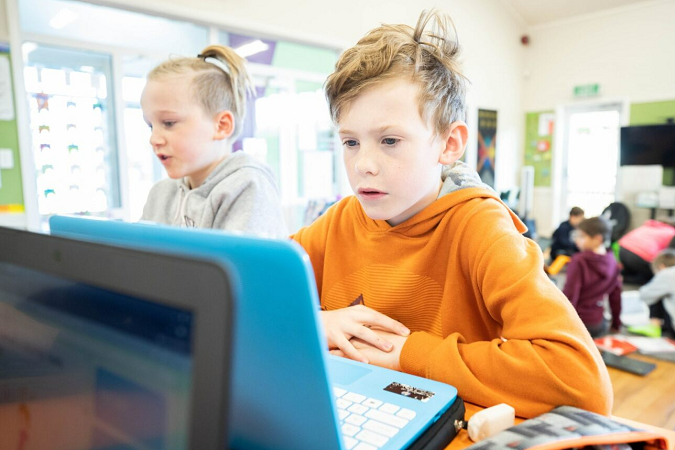 Two Tamariki sitting together in the classroom working on laptops. 