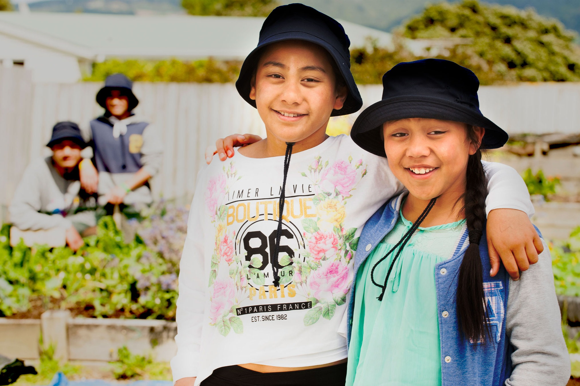 Two children standing in a garden with hats on