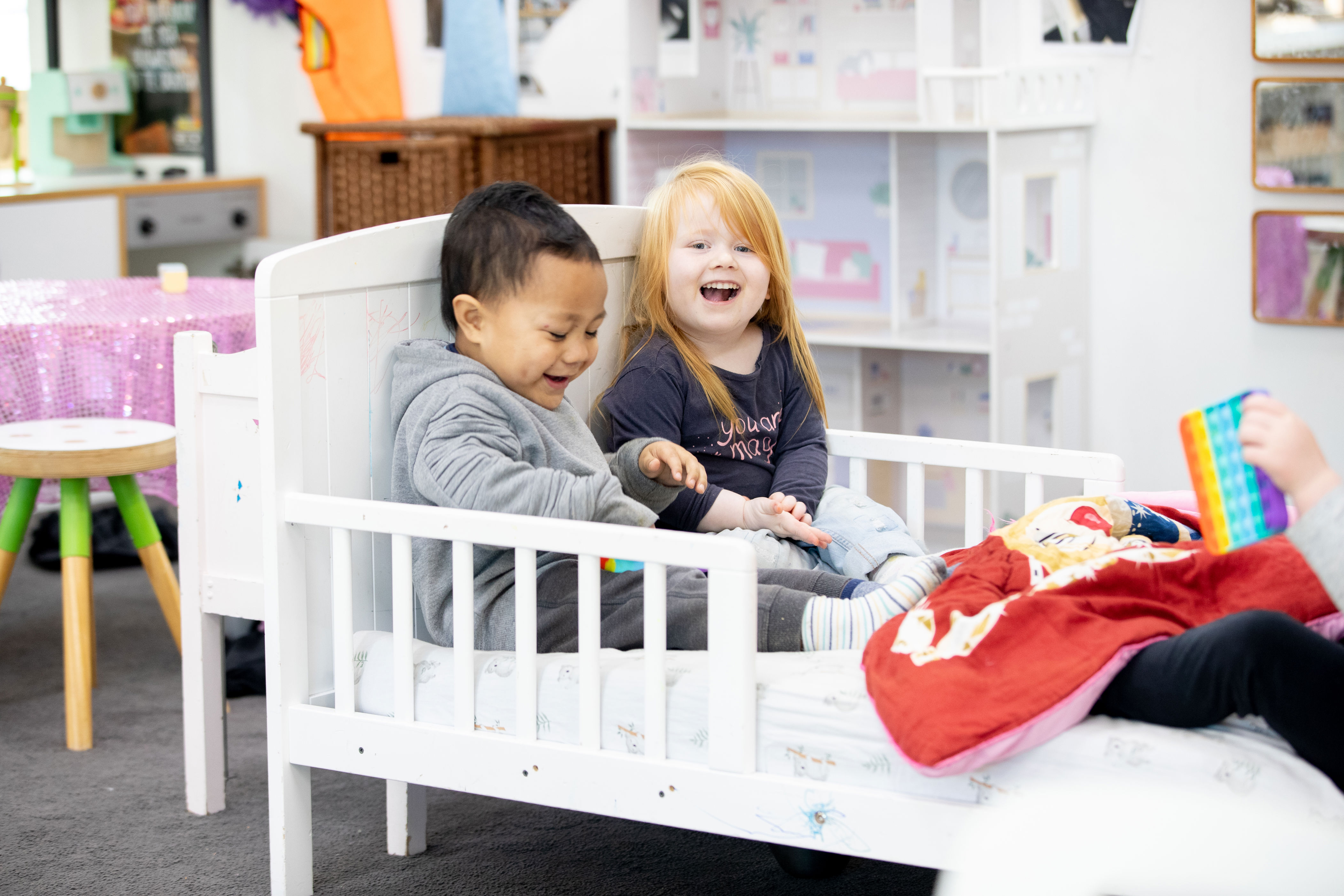 Two children with different length hair playing in a cot together