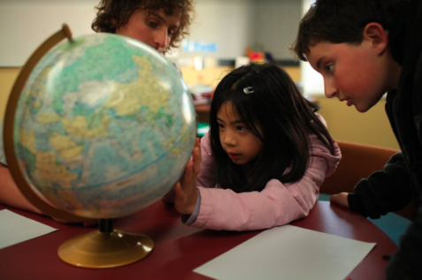 Students and teacher looking at a globe together.