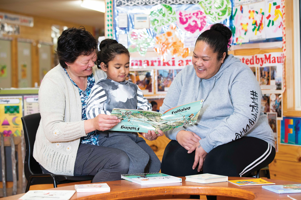 Two kaiako sitting with a young tamariki reading a picture book.