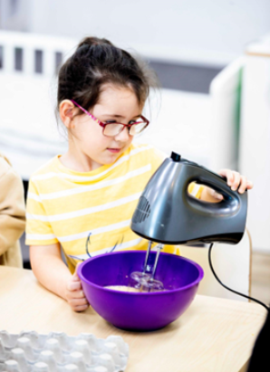 A child is using an electric beater to mix ingredients in a bowl.