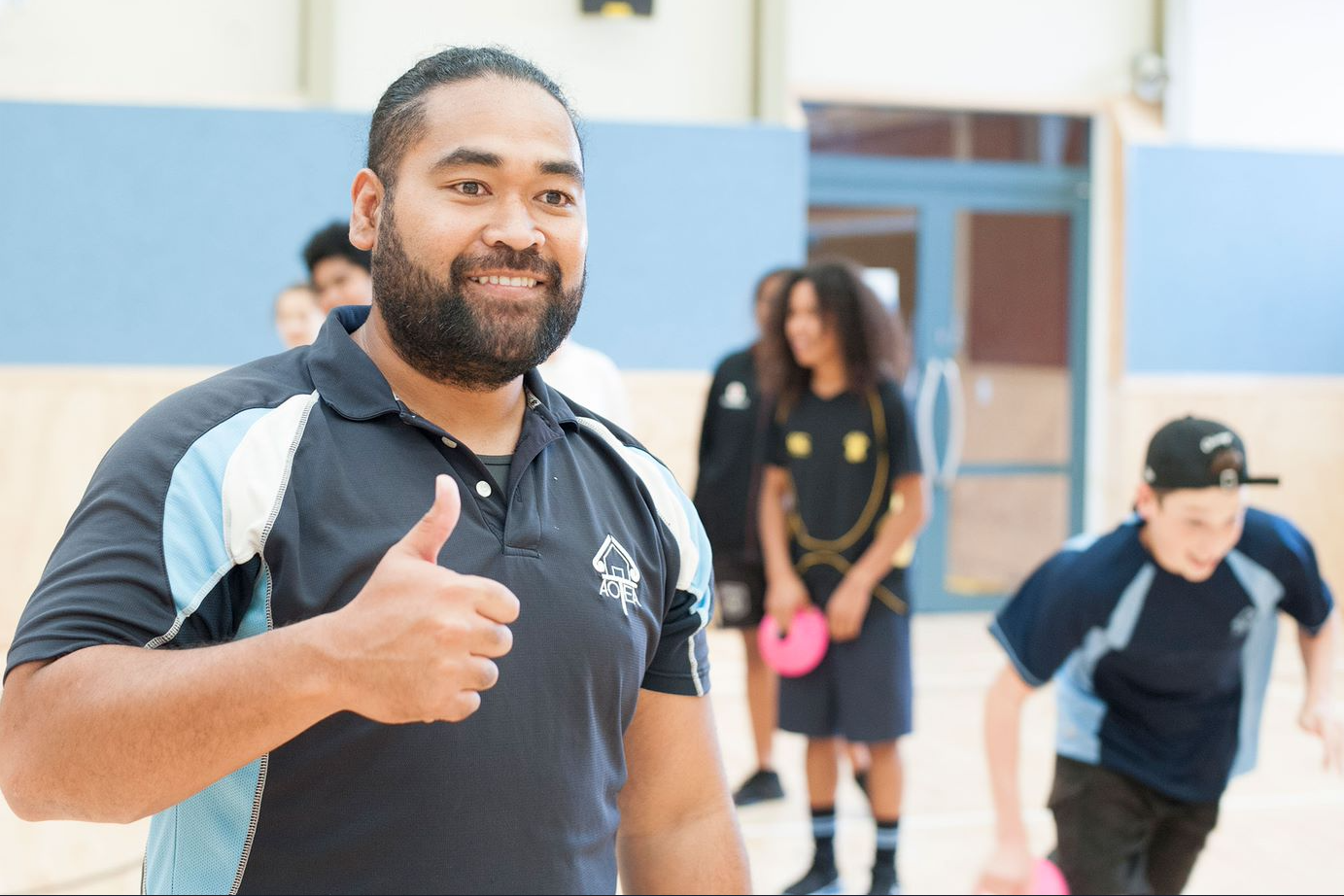 A teacher smiling and giving a thumbs up gesture. 