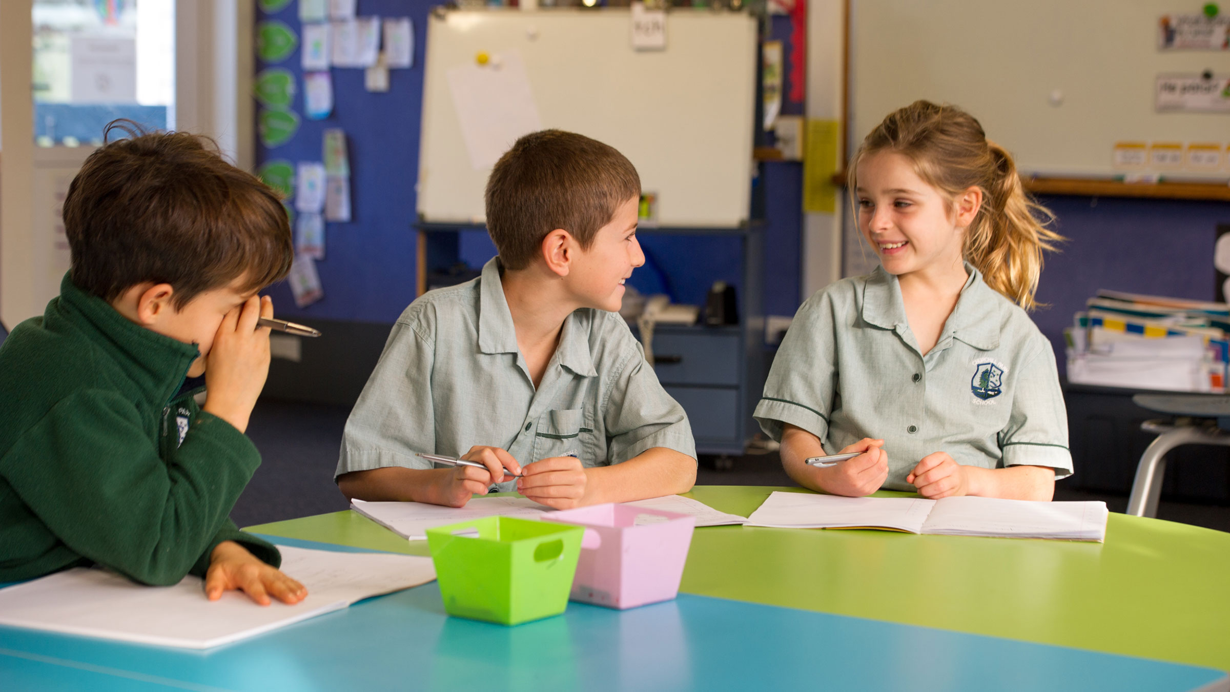 Three students sitting around a table talking to each other. 