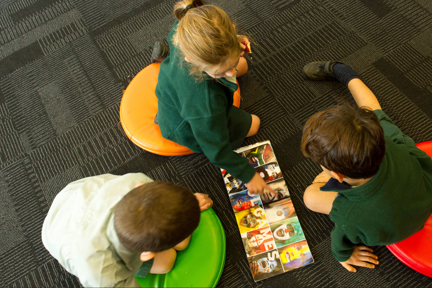 Three children sit on the floor reading a picture book together.