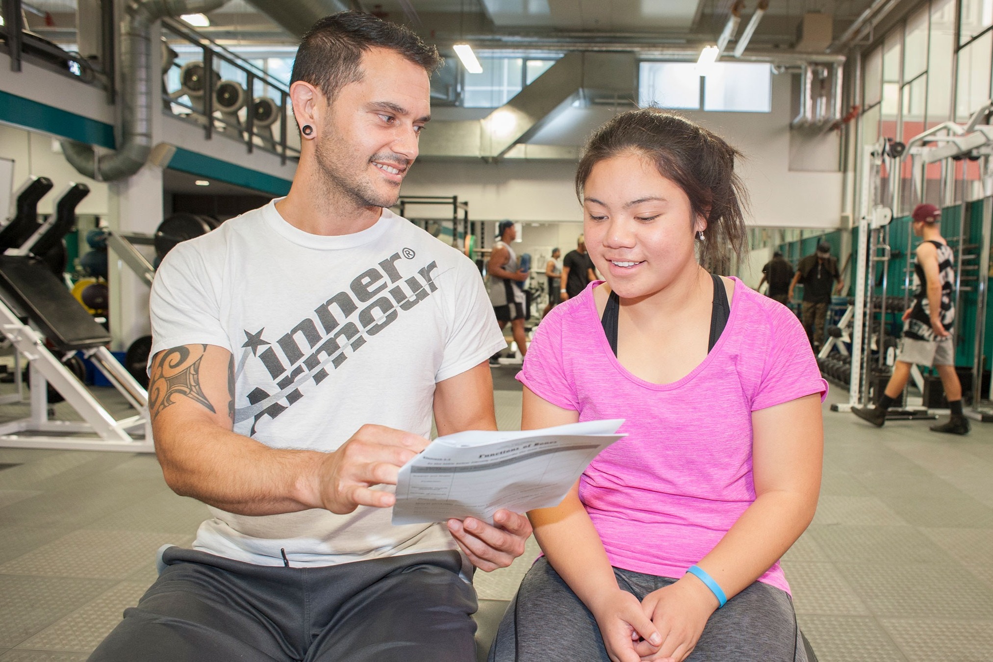 A teacher and student in a gym discussing a worksheet.