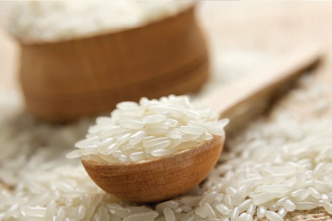 A wooden spoon filled with rice surrounded by rice.