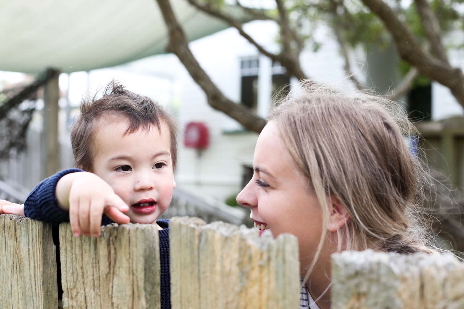Teacher smiling at young child while looking over a fence.