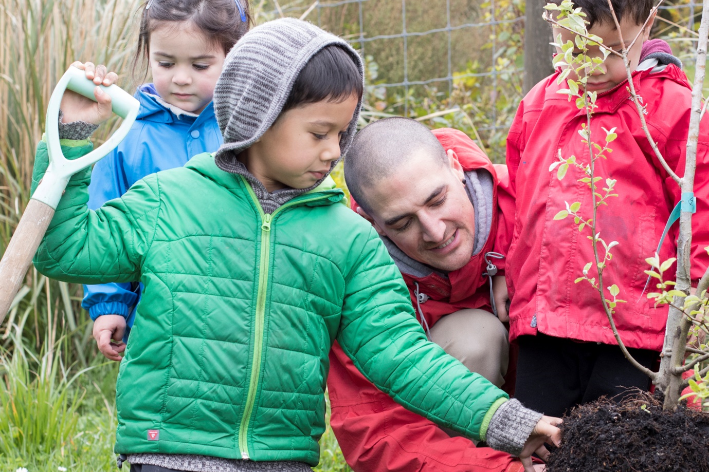 A group of children and a kaiako planting a tree.