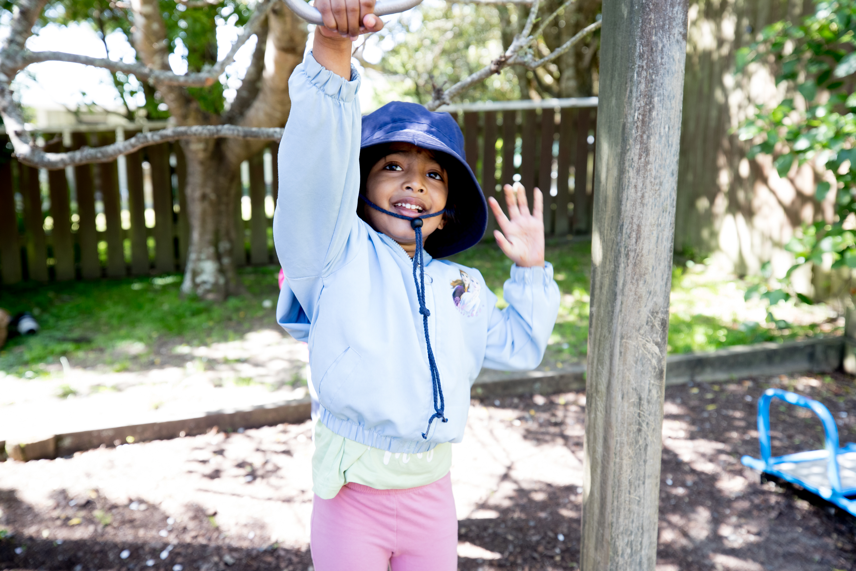 Young tamariki smiles at the camera as they play outside on the playground.