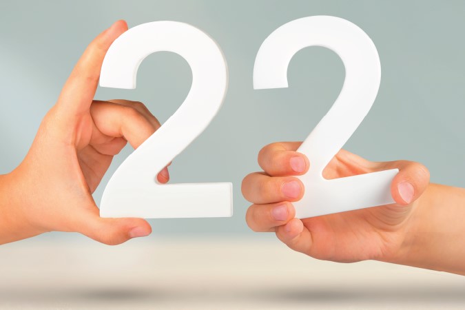 Two hands holding up white numbers, which depict 22. 
