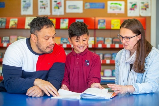 A student sharing his book with two adults.