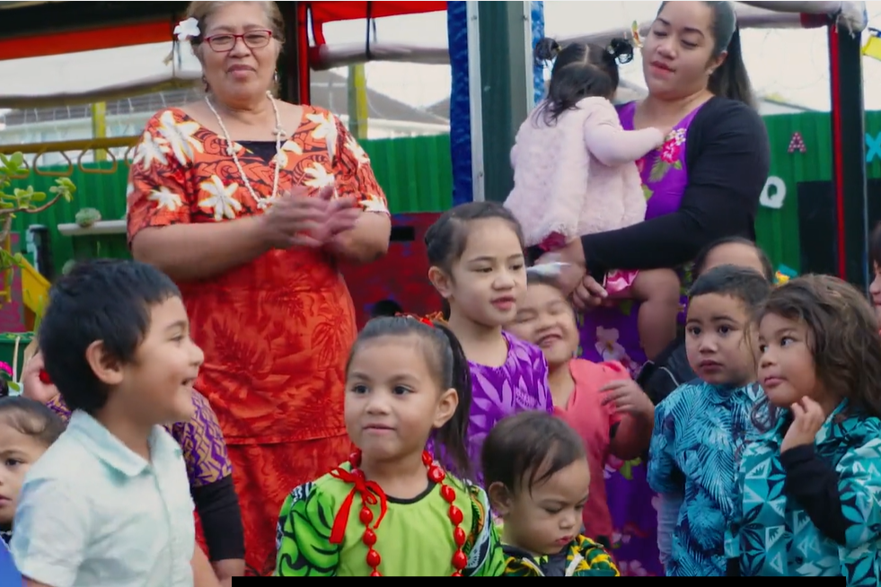 Two teachers and a group of young children stand outside in colourful clothes.