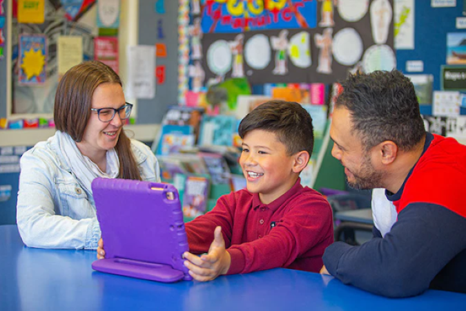 A student and two adults are in discussion, looking at a device.